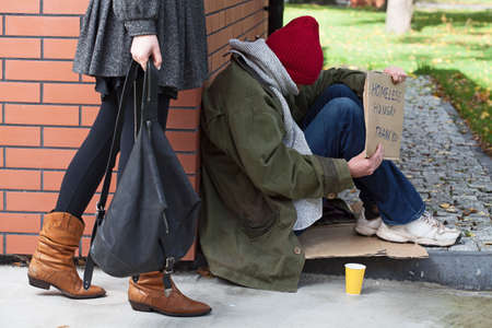 Woman passing by the hungry homeless in needの写真素材
