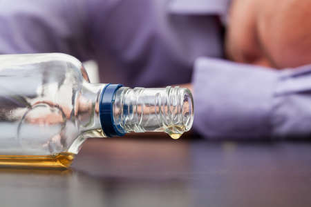 Drunk man sleeping with almost empty bottle of alcoholの写真素材