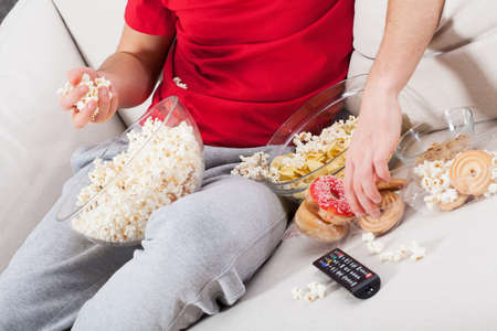 Couch potato watching tv and eating junk foodの写真素材