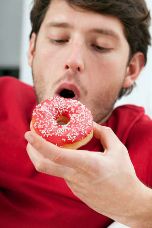 Young handsome man eating delicious donut, vertical