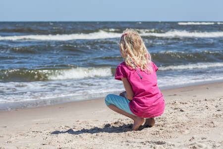 Little girl on a beach watching sea wavesの写真素材
