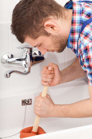 Young plumber unclogging a bathtube drain with plungerの写真素材