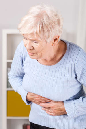 Portrait of elderly woman having stomachache at homeの写真素材