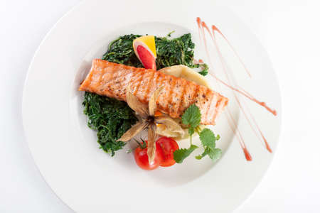 Grilled fish with spinach and tomato on white plateの写真素材