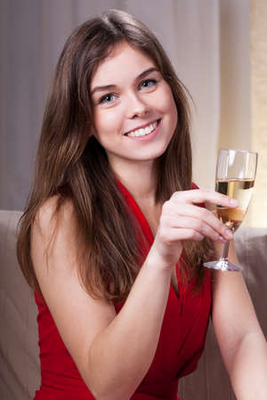 Beauty charming girl in red dress smiling and drinking wineの写真素材