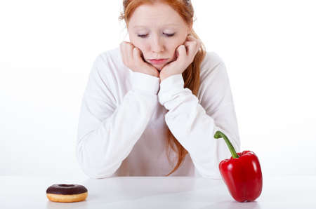 Young girl choosing between doughnut and red peppersの写真素材