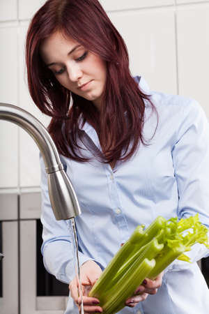Young girl washing celery in kitchen, verticalの写真素材