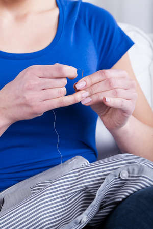 Housewife before sewing a shirt button, vertical
