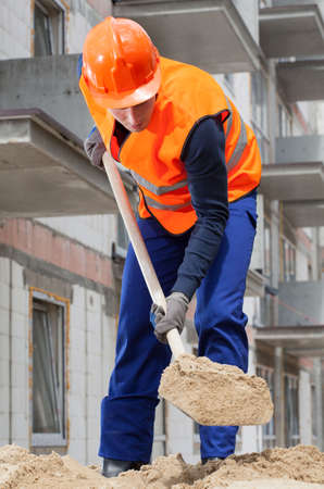 Builder spanning sand with a spade, vertical