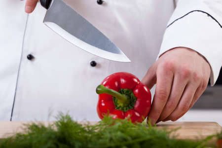 A closeup of a cook cutting a fresh red pepperの写真素材