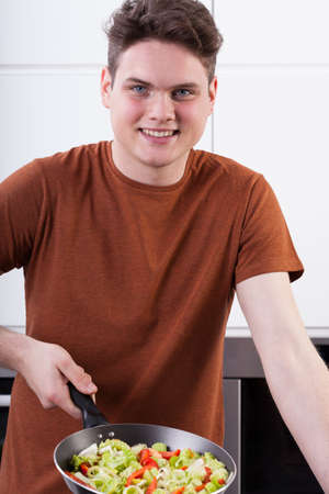 A smiling young man frying vegggies on a panの写真素材