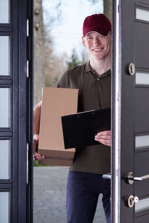 A smiling courier holding a box when entering the houseの写真素材