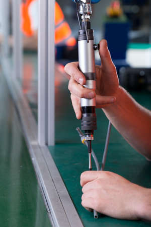 Close-up of hands using pneumatic screwdriver at factoryの写真素材