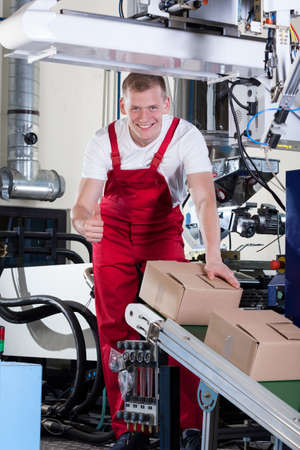 Factory worker showing thumbs up sign next to conveyor belt