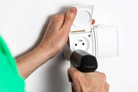Hands with drill tightening a socket into a wall