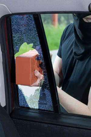 A burglar breaks a window with a brick in the carの写真素材