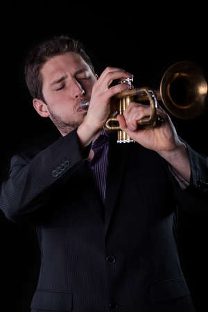 Vertical view of a musician in black suit playing a trumpet