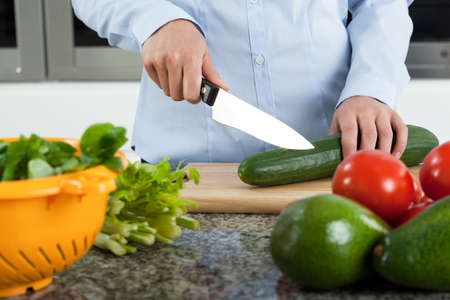 Female hands with knife cutting cucumber for saladの写真素材