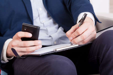 Businessman with smartphone and notes at work 