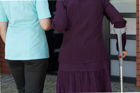 Lady on crutches and nurse coming back homeの写真素材