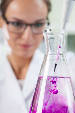 Chemist putting violent liquid into the flask using pipetteの写真素材