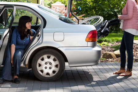 Girl taking wheelchair from car to provide mobility for disabled womanの写真素材