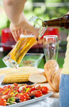 Woman pouring beer to glass on grill partyの写真素材