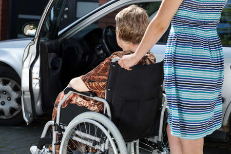 A young woman is carrying an old lady in a wheelchair to the carの写真素材