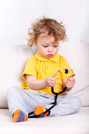 Young kid sitting on a couch and playing with a stethoscpoeの写真素材