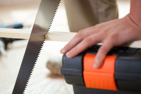 Man's hands using handsaw during renovation, horizontal