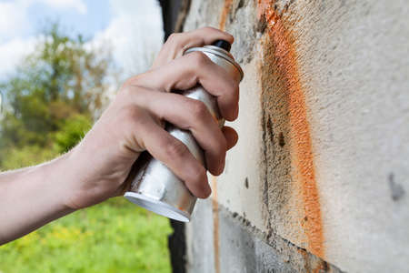 Hand holding graffiti spray, drawing on the wall