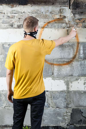 Young hooligan drawing a graffiti on the wallの写真素材