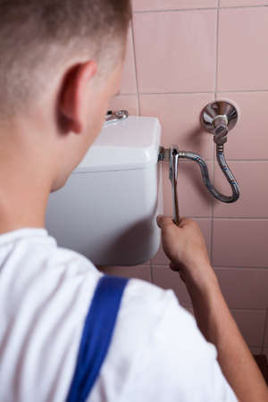 Back view of a plumber fixing a flush toiletの写真素材