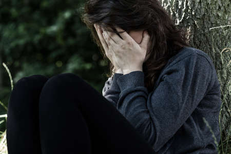 Portrait of young woman crying, sitting under the treeの写真素材
