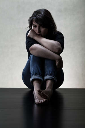 Depressed young woman sitting on the floorの写真素材