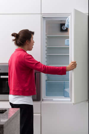 Terrified young woman against the empty fridge