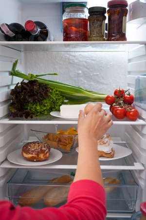 Female hand choosing food from interior of refrigeratorの写真素材