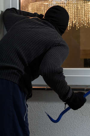 Masked housebreaker with crowbar in front of windowの写真素材