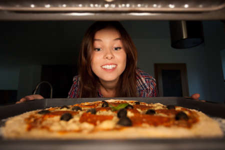 Happy girl putting pizza into oven, horizontalの写真素材
