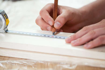 Close-up of a male hands using measuring tape on wooden boardの写真素材