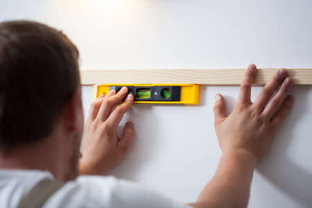 Back view of a man using spirit level at homeの写真素材