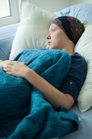 Young woman with headscarf lying in hospital bedの写真素材