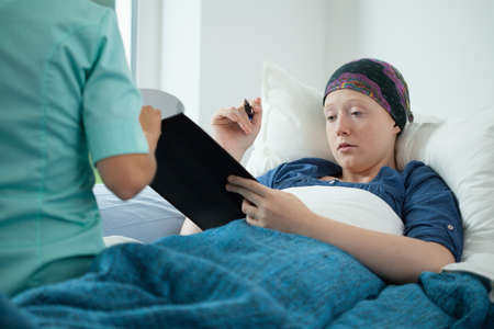 Cancer young woman signing documents in hospitalの写真素材