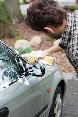 Young man polishing wing window in his car