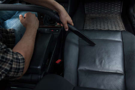 Young man vacuuming grey armchair in his car