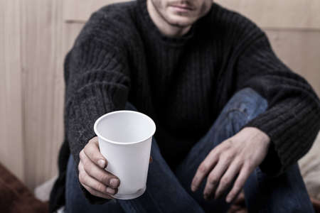 Young homeless man sitting on the ground and asks for helpの写真素材