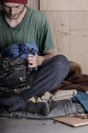 Homeless young man looks a bag of clothesの写真素材