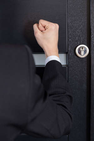 Close-up of clenched fist knocking on the doorの写真素材