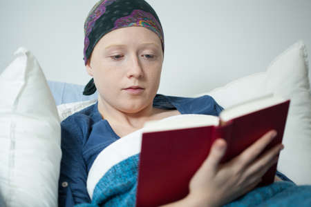 Young cancer woman reading the book in hospital bedの写真素材
