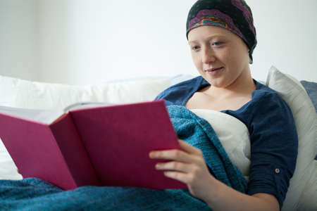 Young sick woman with cancer browses her pink photo albumの写真素材